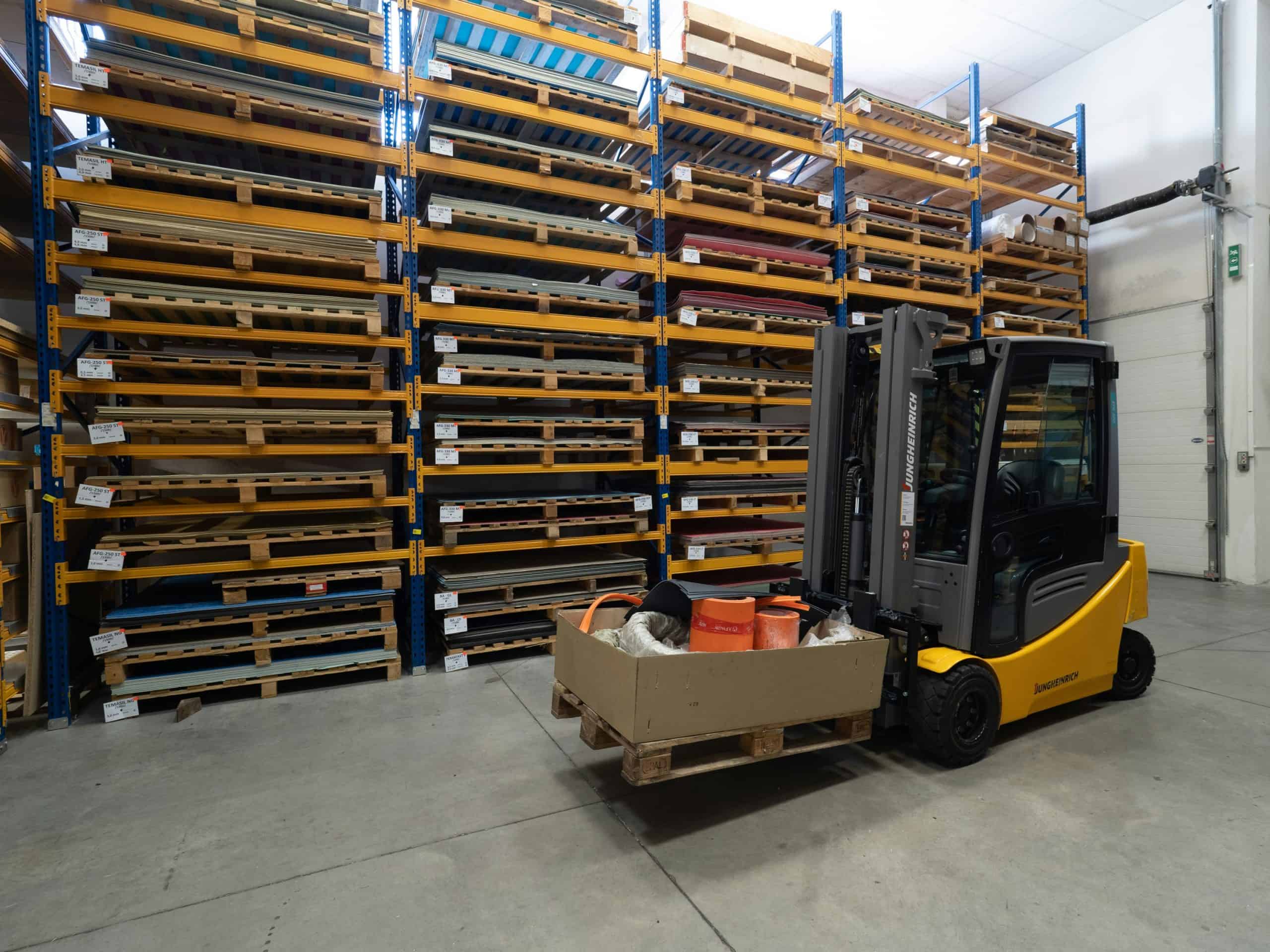 Forklift in warehouse aisle with stacked pallets